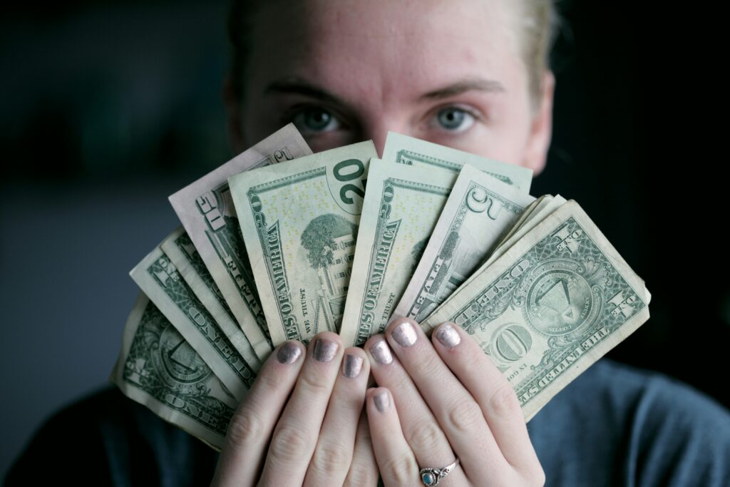 Person with silver nails holding a lot of money fanned out covering their face