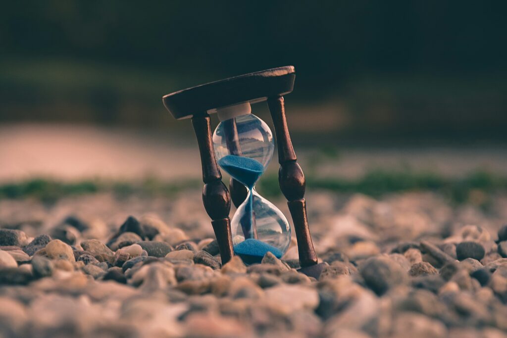 Wooden hourglass with blue sand. Half the time has elapsed and the hourglass is in a sea of pebbles.