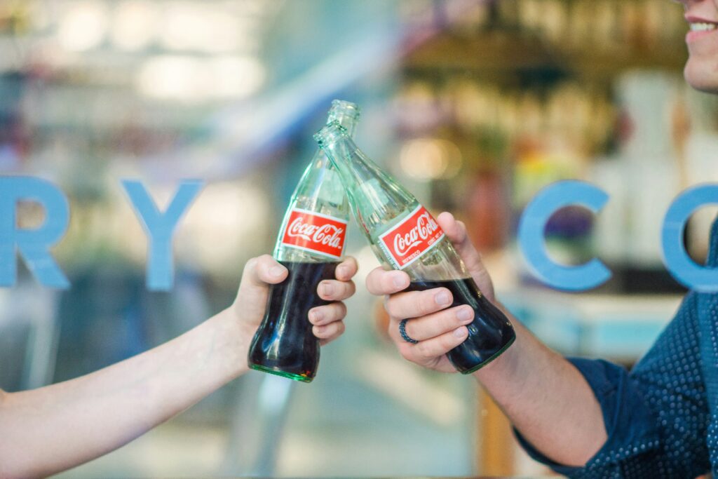 Two people clinking glass CocaCola bottles