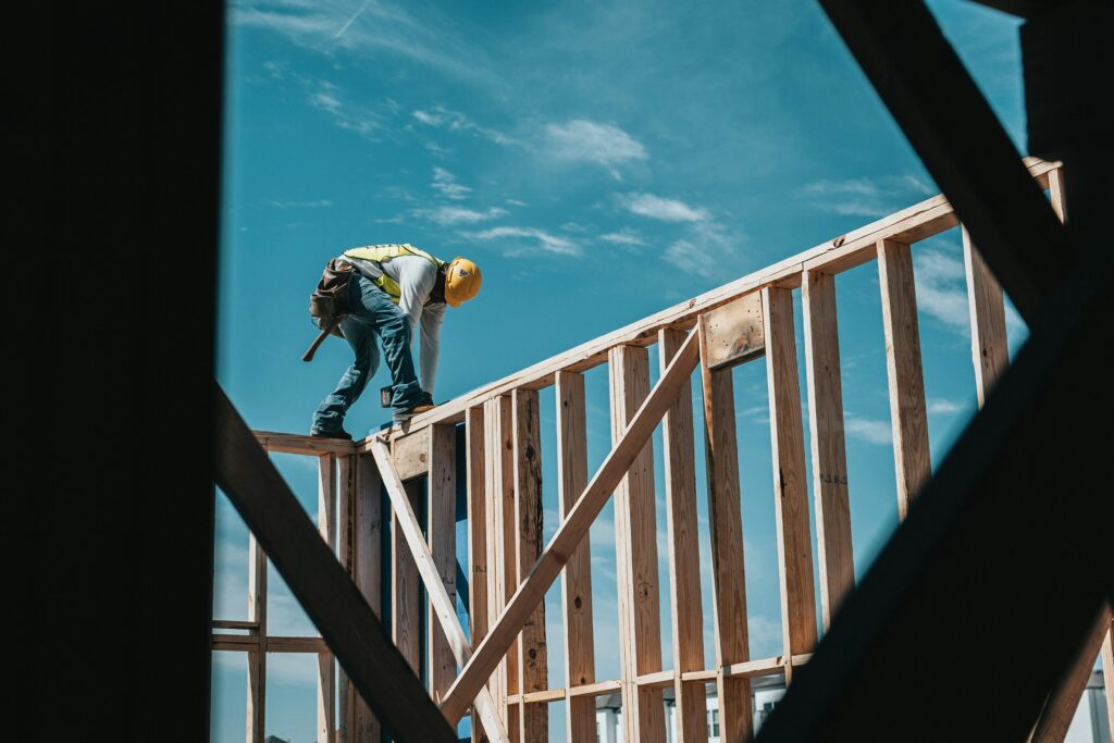 Man in yellow hard hat standing on brown wooden house frame